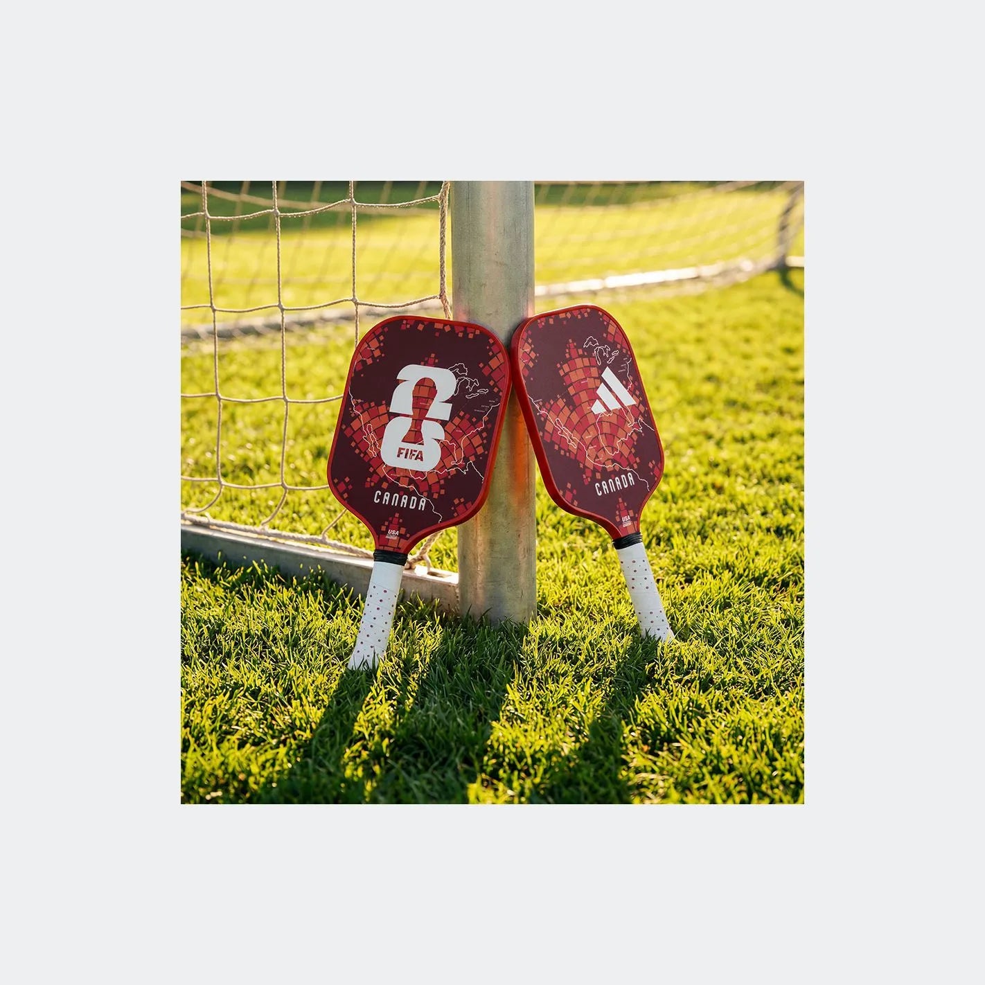 Two red pickleball paddles with white strings leaning against a goalpost on grass.